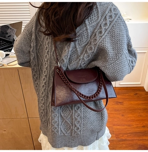 Macro detail of wine red glossy handbag with chain strap on grey knit sweater background