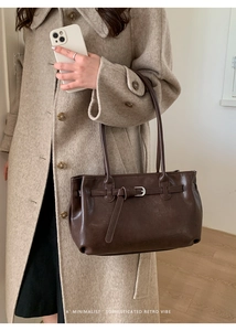 Detail of dark brown vintage leather shoulder bag with buckle strap on beige wool coat