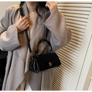 Close-up of black glossy small square crossbody bag with gold twist lock and knot handle