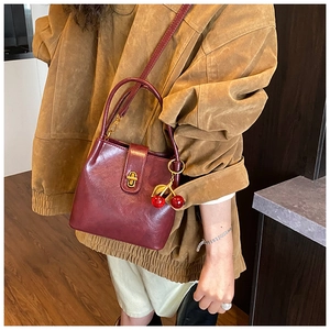 Detail of burgundy leather bucket bag with gold hardware and a cherry charm