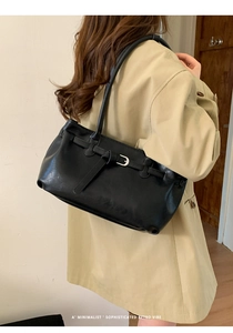 Detailed view of vintage black leather tote bag with buckle strap on beige trench coat