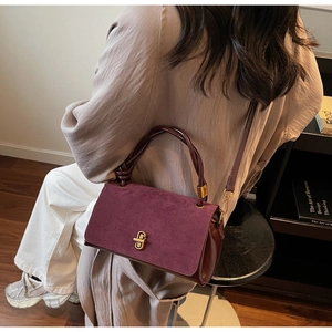 Detail of burgundy flap handbag with suede texture, gold lock, and adjustable strap