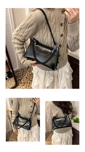 Detail view of black patent leather baguette bag with thick decorative chain and long strap