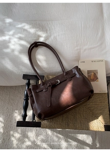 Detail of dark brown leather tote bag with vintage strap buckle on a woven wooden chair