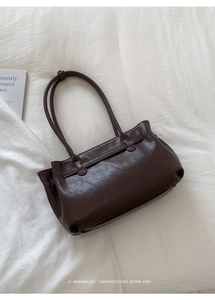 Detail of deep brown retro tote bag with smooth faux leather texture on white bedding