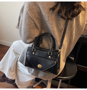 Rear view of a model wearing a black glossy leather satchel with gold hardware accents