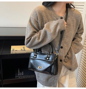 Detail of black leather handbag featuring a golden cylindrical twist lock and flap design
