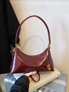Sac demi-lune en cuir verni bordeaux avec chaîne dorée sur une valise argentée