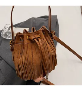 Détail d'un sac seau marron à franges avec cordon sur un magazine de mode chic
