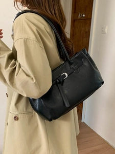 Classic black leather tote bag with vintage buckle detail worn by a model in a trench coat