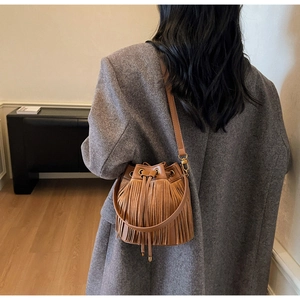 Sac seau à franges marron avec cordon de serrage et détails dorés porté à l'épaule