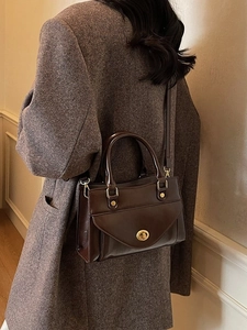 Vintage dark brown leather handbag with gold oval clasp shown in a lifestyle pose