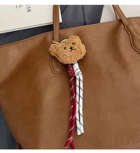 Detail of plush bear charm with braided rope on a brown leather tote bag