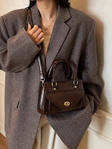 Classic dark brown leather handbag with gold lock and rivet details on brown blazer