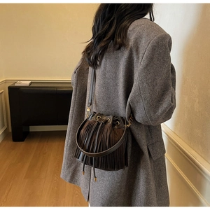 Détail d'un sac seau marron foncé à franges sur un mannequin féminin élégant en intérieur