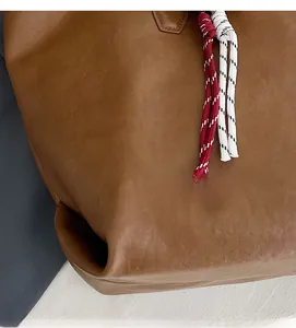 Close-up of brown leather tote bag with red and white braided rope detail and matte finish