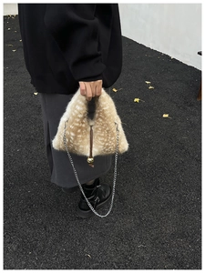 Detail of plush faux fur handbag with white spots, chain strap, and golden bell charm