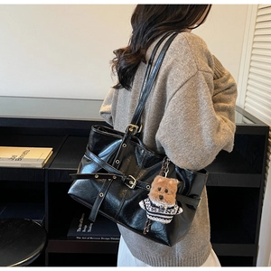 Detail of glossy black leather tote bag with metallic buckles and brown dog plush charm