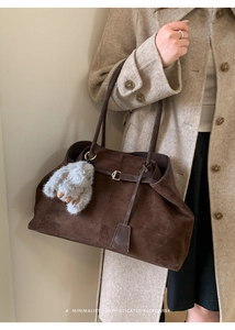 Detailed view of large brown suede tote bag with decorative buckle and plush bunny charm