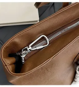 Detail of silver smooth zipper hardware on brown leather tote bag with carabiner puller