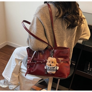Detail of wine red glossy shoulder bag featuring buckle straps and a cute teddy bear charm