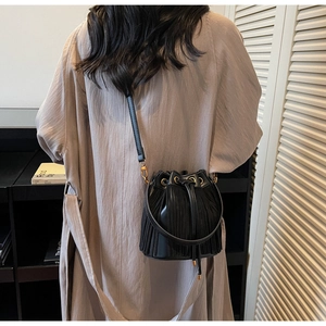 Gros plan du sac seau à franges noir avec œillets métalliques dorés et fermeture à cordon