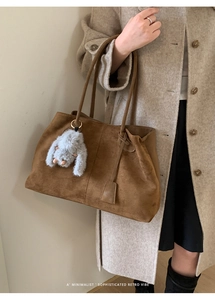 Detail of brown suede tote bag featuring a cute plush bunny charm and minimal long strap