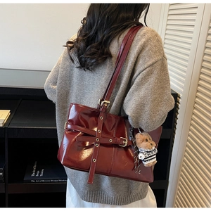 Close-up of a glossy dark red leather tote bag featuring metal buckles and a teddy bear charm