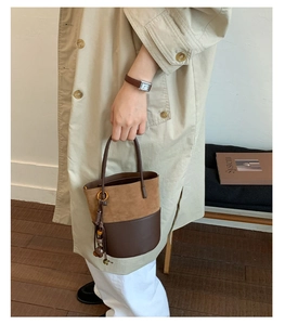 Detail of two-tone bucket bag featuring brown suede stitching and beaded tassel charm