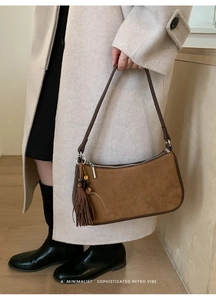 Detail of suede crossbody bag featuring tassel charm and silver zipper closure