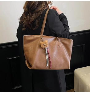 Brown leather tote bag with teddy bear pendant shown on a model's shoulder for daily use