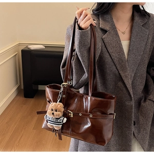 Detail of dark brown glossy leather tote bag with gold buckle and bear charm accessory