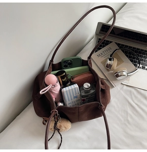 Top view of large brown suede tote bag filled with personal essentials like a phone and umbrella