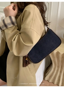 Detail of navy blue suede handbag with brown leather trim and tassel on a khaki coat