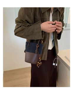 Detail view of mini two-tone bucket bag featuring blue suede and brown leather with tassels
