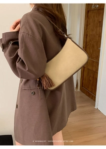 Detail of beige suede baguette bag with brown trim and tassel worn by a model