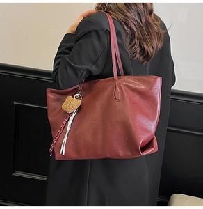 Detail of burgundy tote bag with plush bear charm and woven strap on model's shoulder