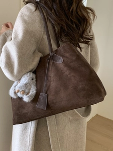 Deep brown suede tote bag with plush charm shown on a model in a beige wool coat
