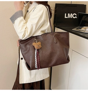 Detail view of a large brown matte leather tote bag with a plush bear charm and tassels