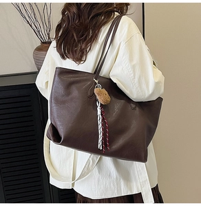 Detailed side view of a large brown tote bag with cute bear charm and woven tassels