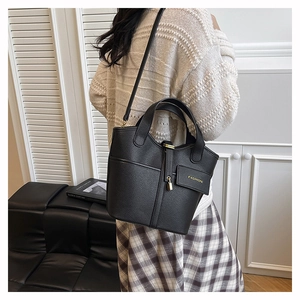 Close-up of black bucket bag with leather texture, dual handles and fashion tag detail