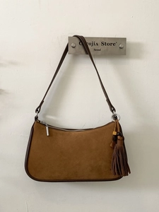 Brown suede baguette bag with leather trim and bohemian tassel charm on wall hook