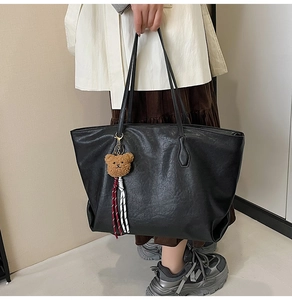 Close-up of black matte tote bag with plush bear charm and detailed leather texture