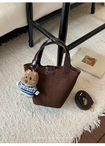 Detail of retro suede bucket bag with bear charm and adjustable shoulder strap