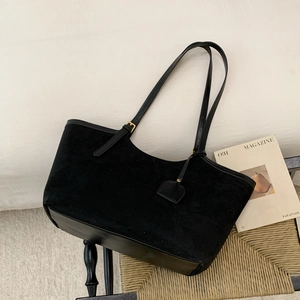 Détail d'un sac cabas en daim noir avec boucles dorées posé sur une chaise tressée