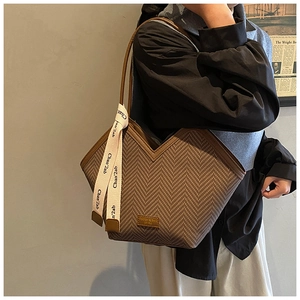 Detailed close-up of brown houndstooth tote bag with leather trim and decorative ribbon
