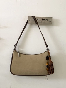 Khaki suede square shoulder bag with brown piping and tassel charm hanging on wall