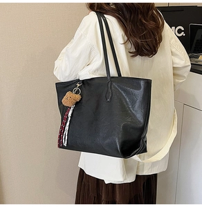 Detail of a large black tote bag with plush bear charm and woven rope on shoulder