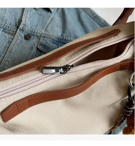Close-up of smooth metal zipper and brown leather trim on beige canvas tote bag