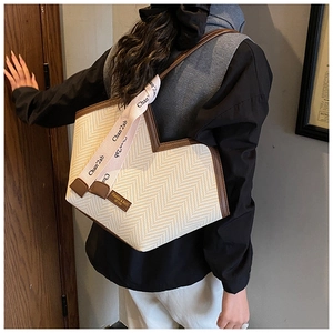 Detail of cream woven tote bag with V-shaped opening and brown leather trim on a model